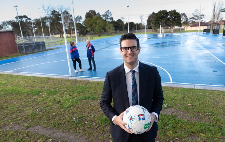 Councillor Tim Dark holding a netball in front of two people talking on a netball court