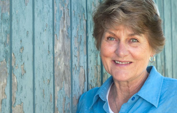 smiling senior woman smiling in front of a wooden wall