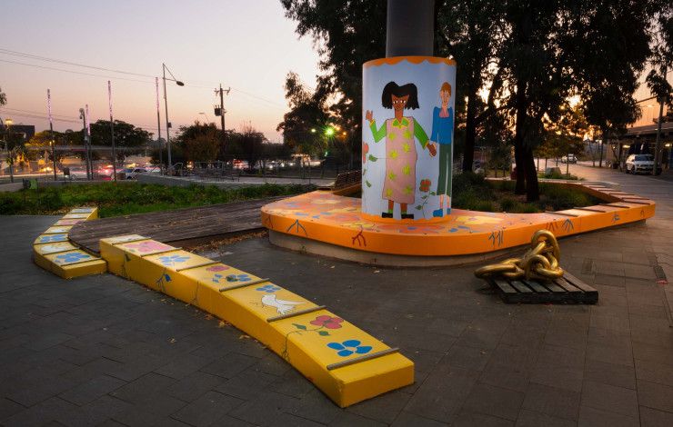 Seating and a light box in a public space decorated with colourful paintings of people