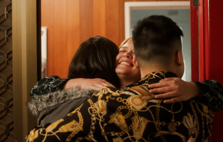 Three young people embracing in the doorway to a suburban house