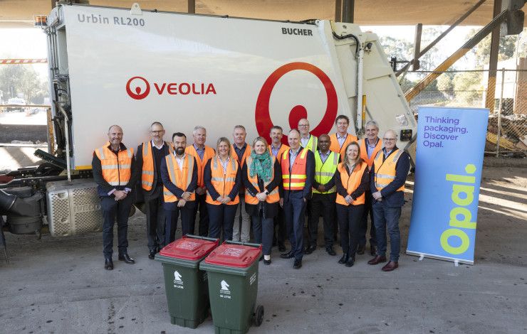 A group of people in high vis vests stood in front of a garbage truck.