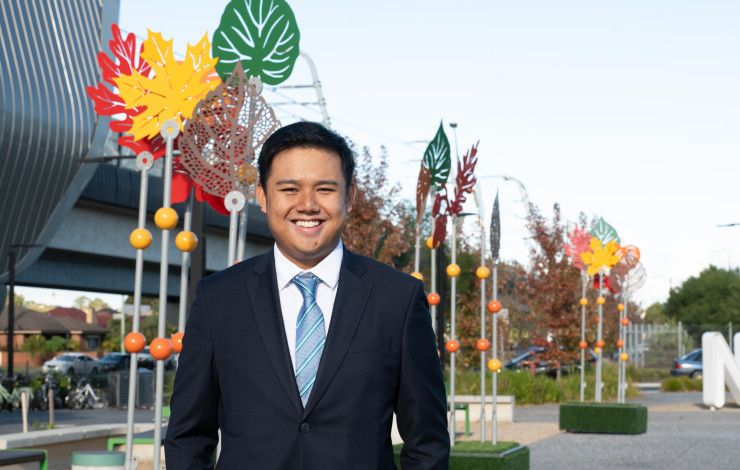 A man in a suit and tie smiles at the camera in front of colourful metal sculptures