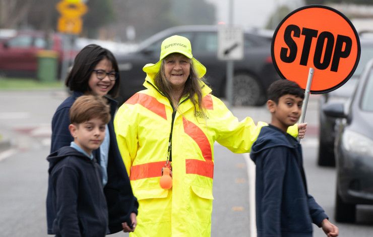 A school crossing supervisor holding a stop sign while three children cross the road in front of her
