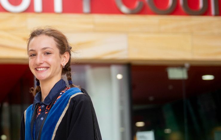 A girl dressed in blue robes smiles at the camera while standing side on