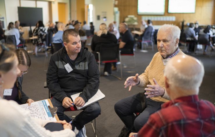People sitting in a circle having a chat in a room full of people sitting in groups talking.