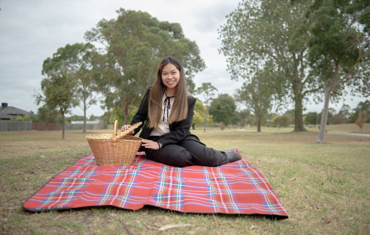 Smiling woman sitting on a picnic rug while opening a wicker picnic basket