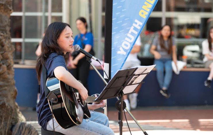 A woman playing guitar while she sings into a microphone in a public space