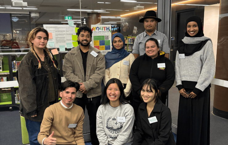 A group of smiling youth some in a line behind others kneeling on the ground.