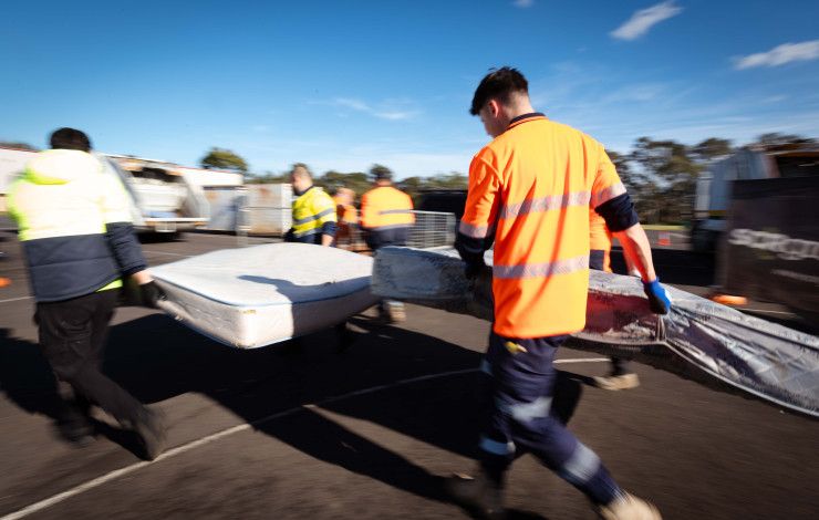 People in hi-vis carrying a mattress