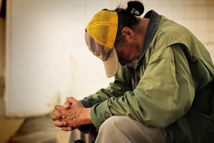 a person with their head down wearing very worn clothing