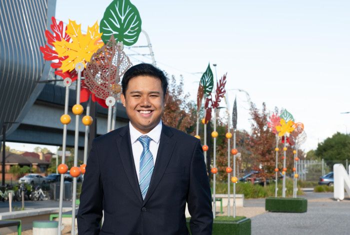 A man in a suit and tie smiles at the camera in front of colourful metal sculptures