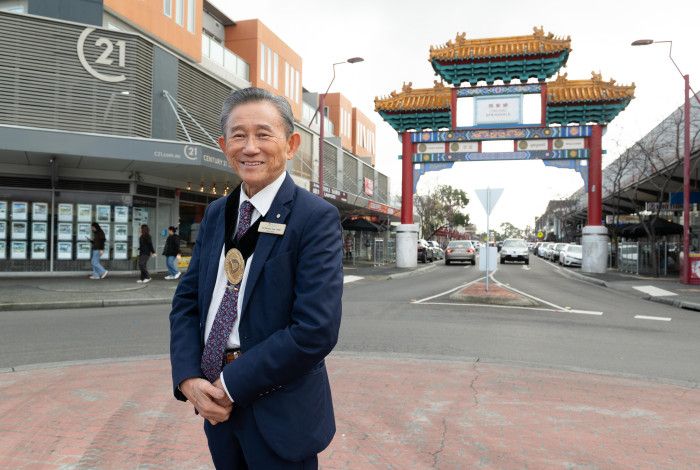 A man smiling at the camera, in the background is a large ornate Asian gateway