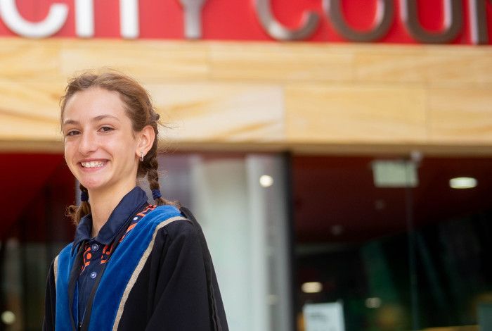 A girl dressed in blue robes smiles at the camera while standing side on