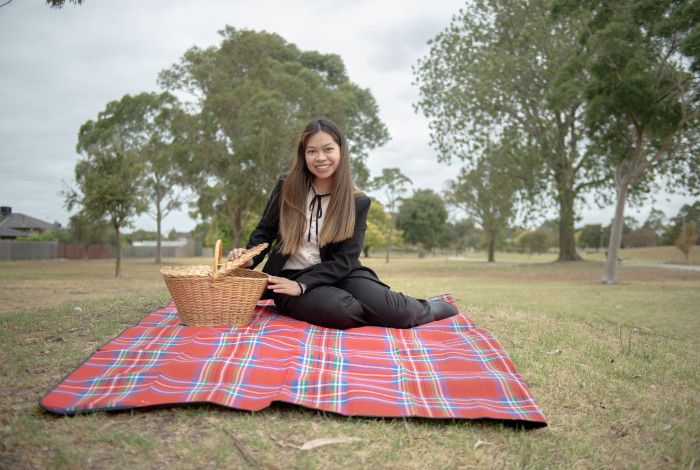 Smiling woman sitting on a picnic rug while opening a wicker picnic basket