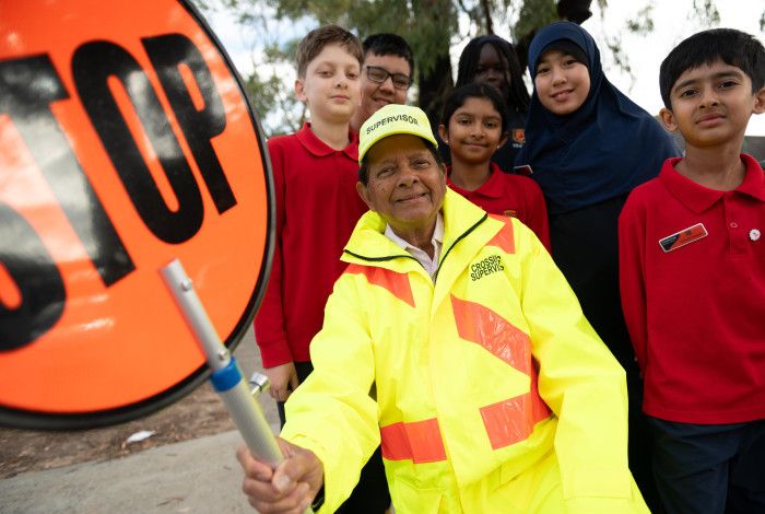A smiling man dressed in high vis holding a stop sign while surrounded by smiling school children