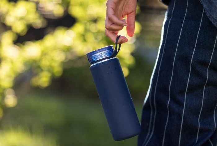 A blue reusable water bottle hanging from the hand of someone walking in a park
