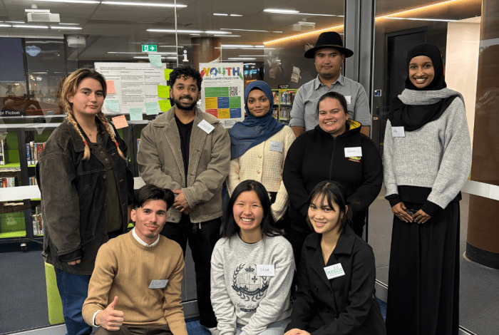 A group of smiling youth some in a line behind others kneeling on the ground.