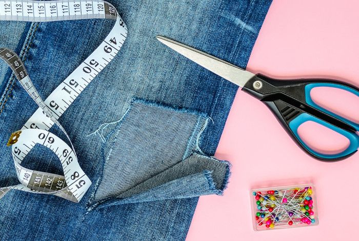 Someone repairing jeans with scissors and measuring tappe