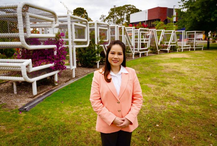 A woman dressed in a light pink blazer standing in front of a metal sculpture spelling out Springvale