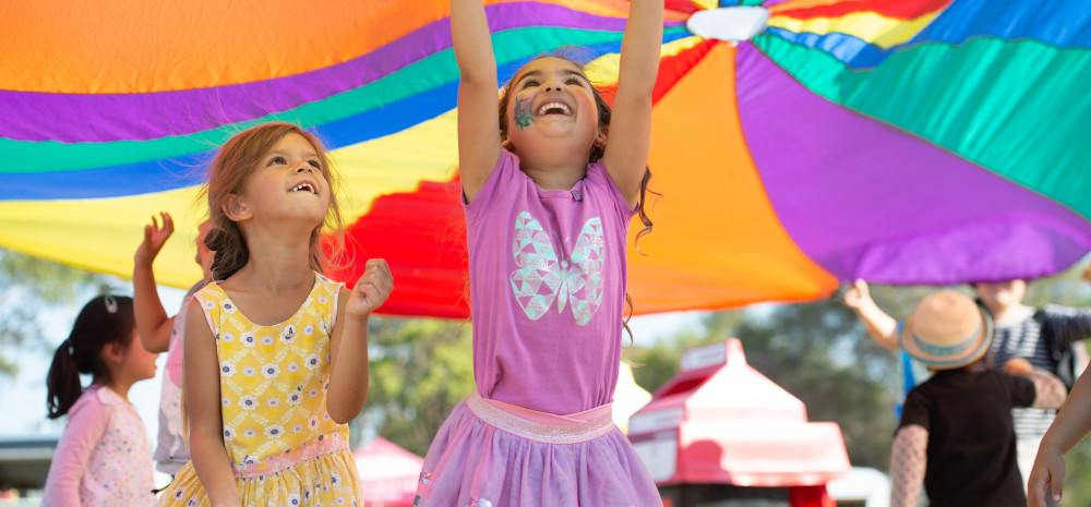 Two children playing under a rainbow parachute