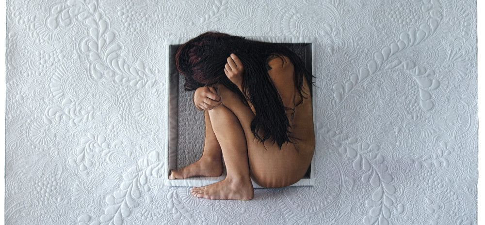 A woman crouched inside a hole in a white, textured wall.