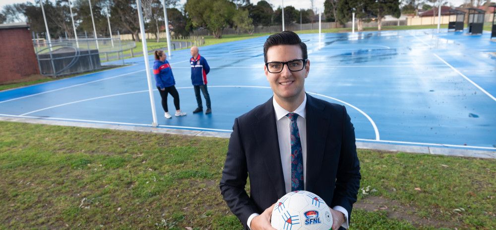 Councillor Tim Dark holding a netball in front of two people talking on a netball court