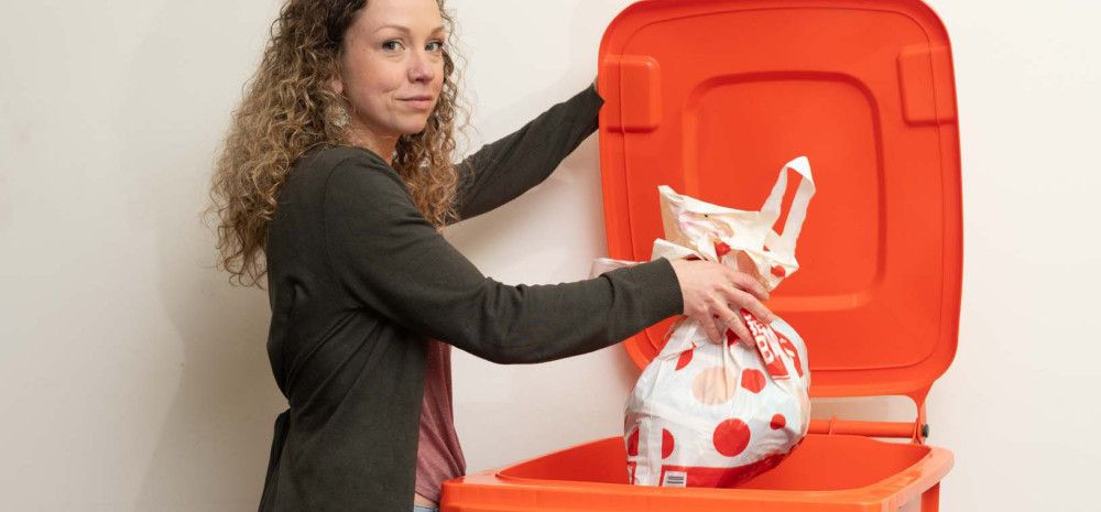 A woman putting soft plastics into an orange recycling bin