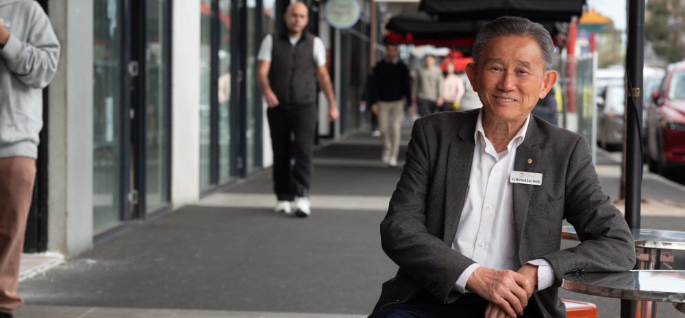 Councillor Richard Lim sitting on street furniture in Springvale