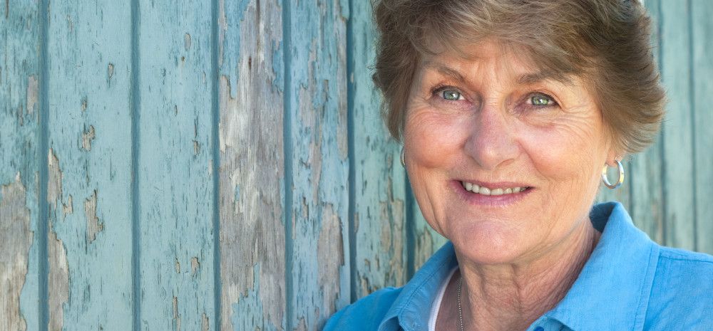 smiling senior woman smiling in front of a wooden wall