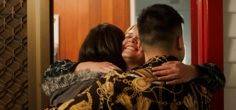 Three young people embracing in the doorway to a suburban house