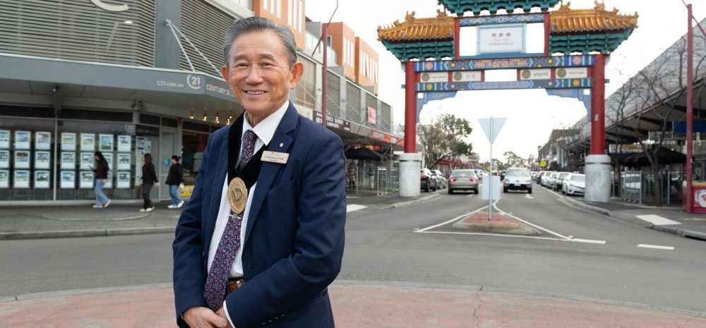 A man smiling at the camera, in the background is a large ornate Asian gateway