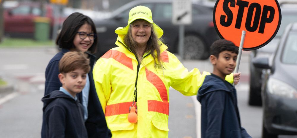 A school crossing supervisor holding a stop sign while three children cross the road in front of her