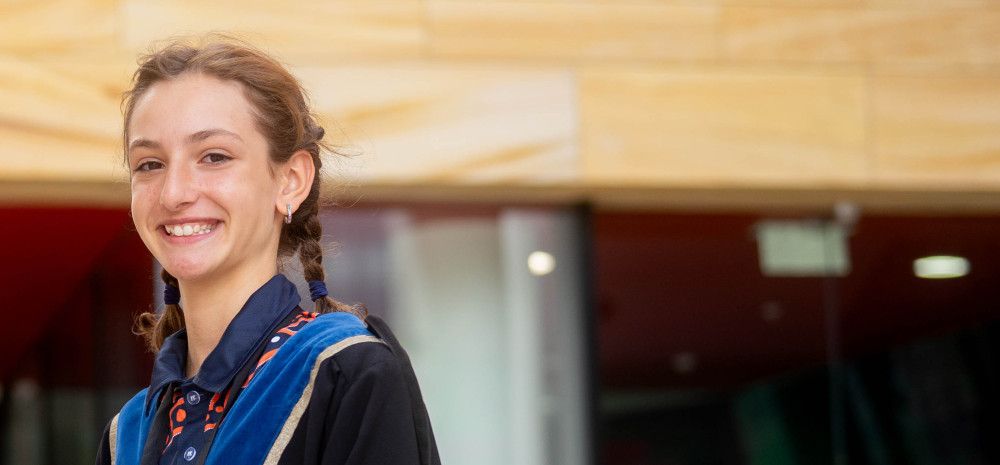 A girl dressed in blue robes smiles at the camera while standing side on