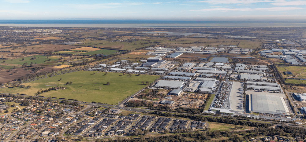 A view from above of a large suburb including housing, an industrial estate and open green paddocks