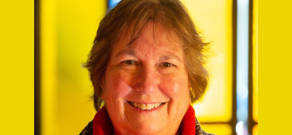 A smiling woman with short hair in front of a stained glass window