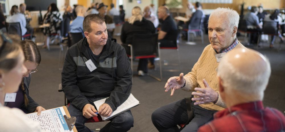 People sitting in a circle having a chat in a room full of people sitting in groups talking.