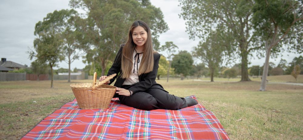 Smiling woman sitting on a picnic rug while opening a wicker picnic basket