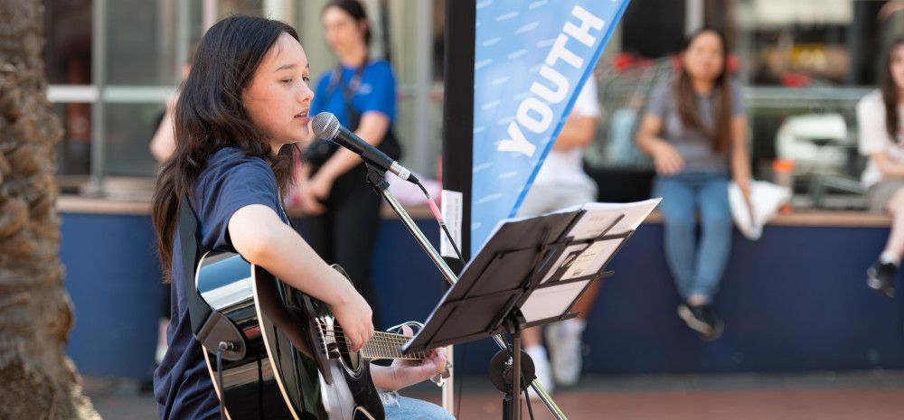 A woman playing guitar while she sings into a microphone in a public space
