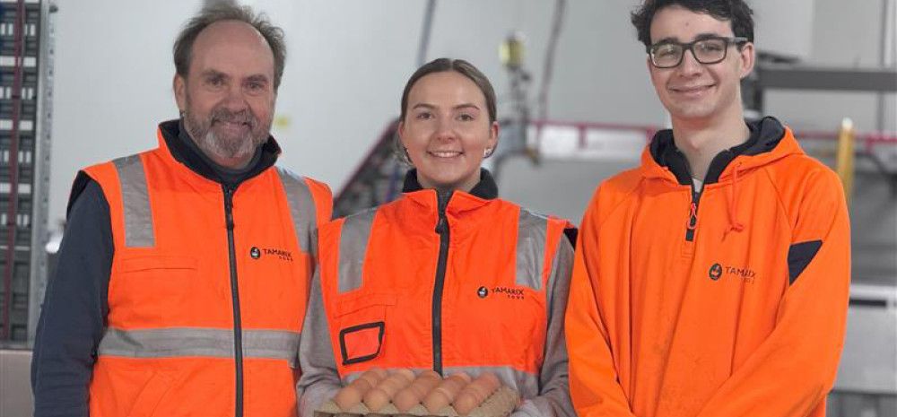 Three people smiling and holding a carton of eggs
