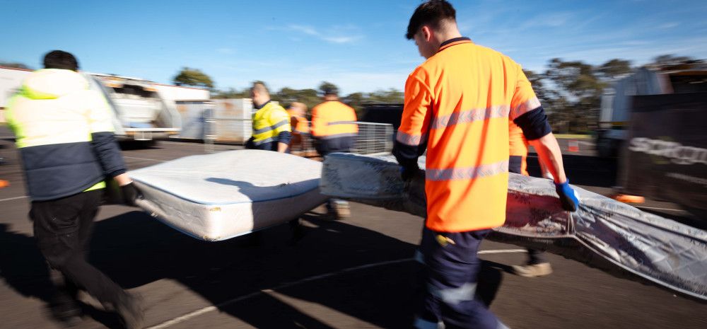 People in hi-vis carrying a mattress