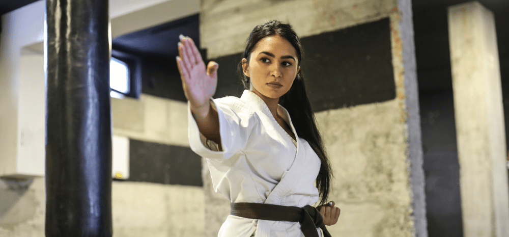 Woman in a white karate uniform with black belt hitting a punching bag