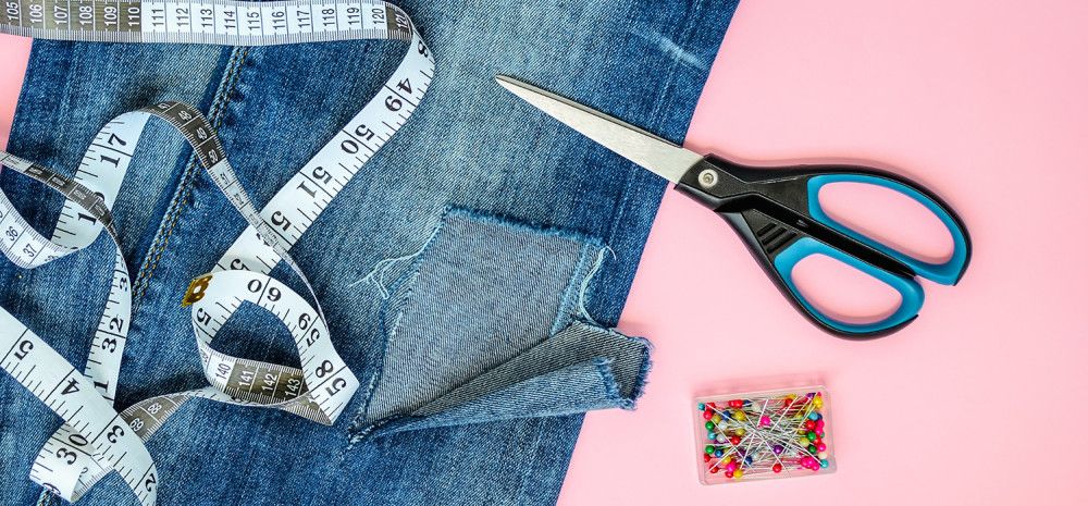 Someone repairing jeans with scissors and measuring tappe