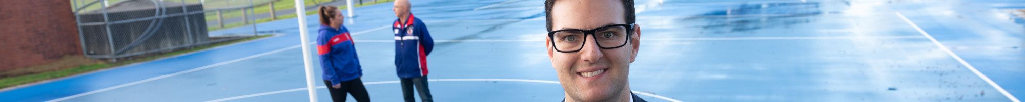 Councillor Tim Dark holding a netball in front of two people talking on a netball court