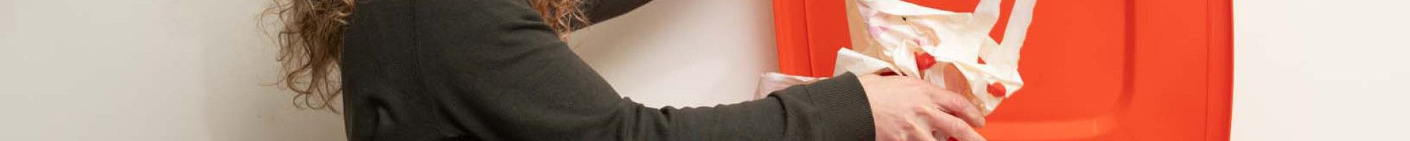 A woman putting soft plastics into an orange recycling bin