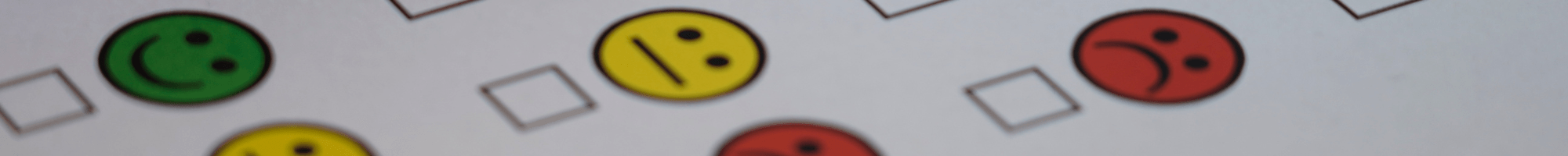 Green, yellow and red smiley icons on paper. A person is ticking the green happy icon.