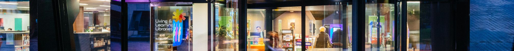 Revolving door below a green ceiling and a lit-up sign that says Library