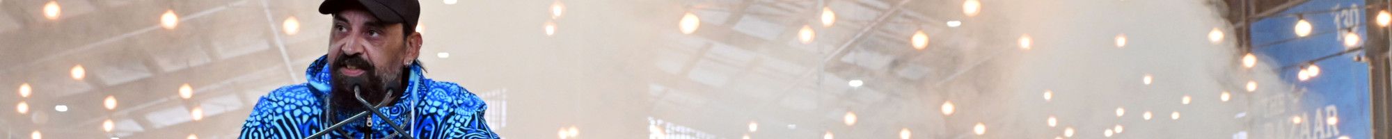 A man stands behind a lectern as smoke creates and almost white background behind him.