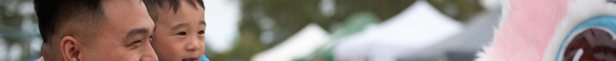 A man holds a small child up while they look into the eyes of a giant pink bunny