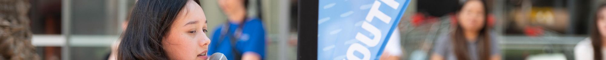 A woman playing guitar while she sings into a microphone in a public space