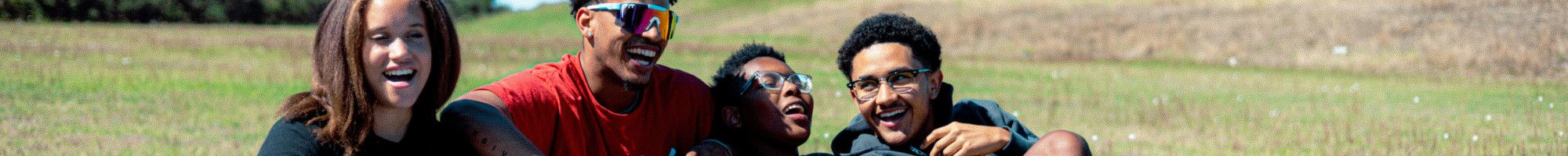 Four young people sitting together and laughing on a grassy hill.